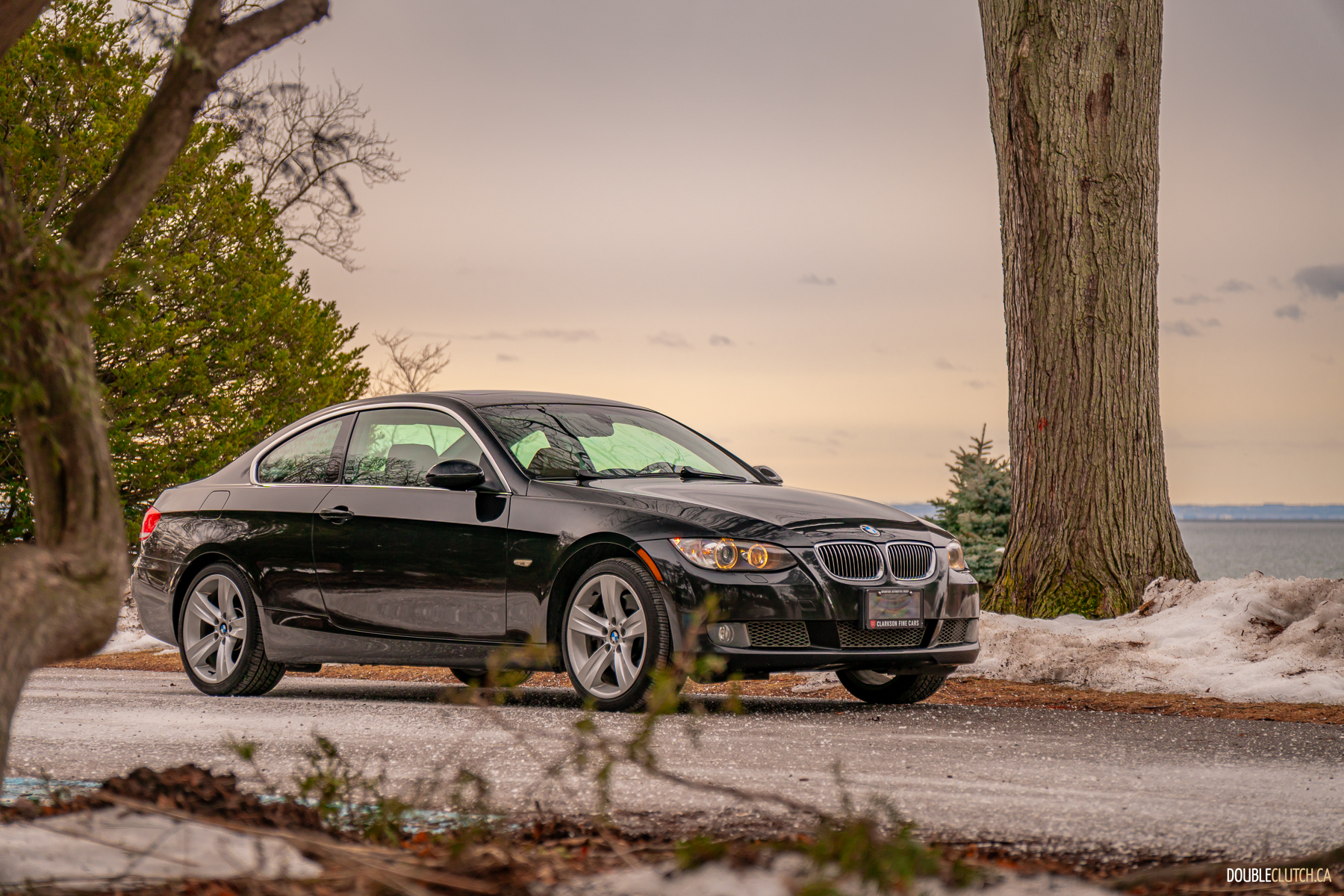 Front quarter view of a black 2008 BMW 335i Coupe on a cloudy day with trees in the background