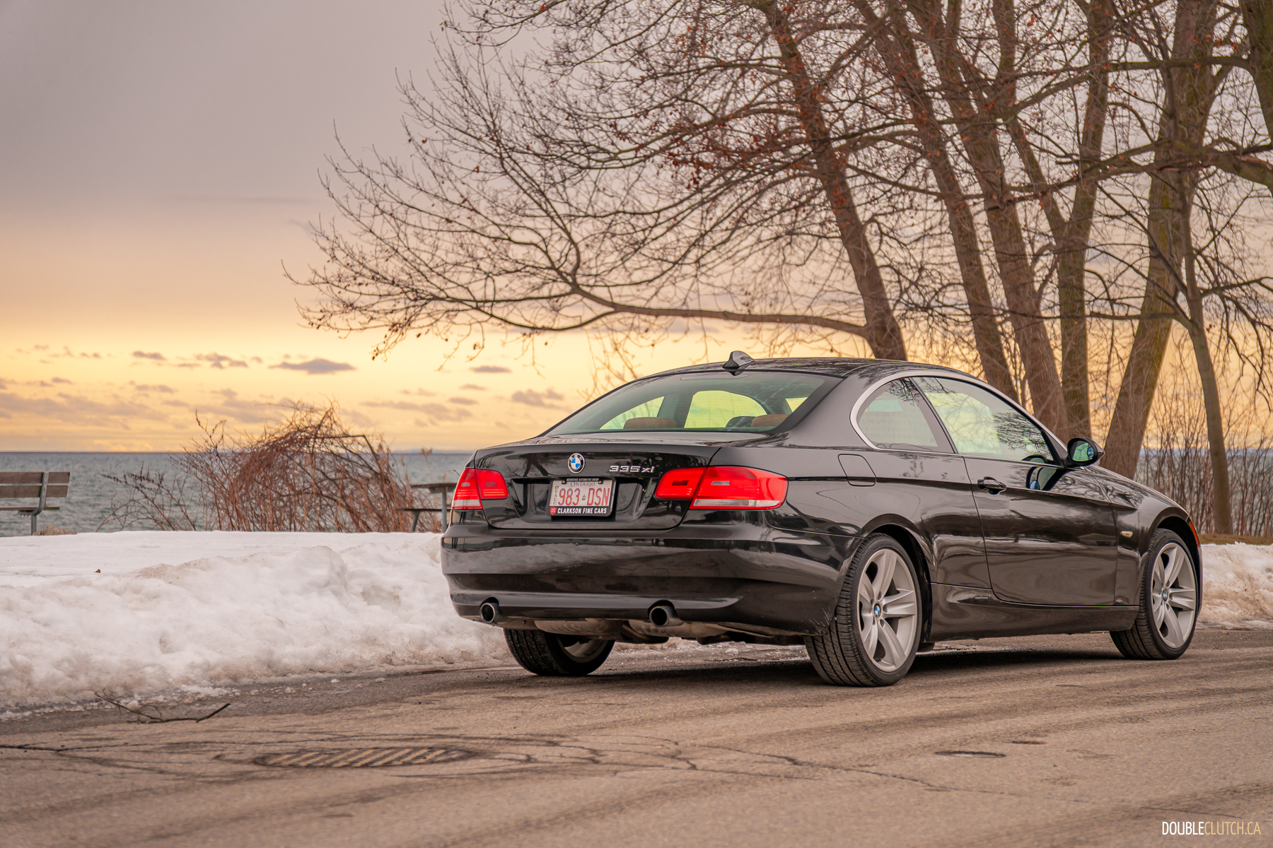 Rear quarter view of a black 2008 BMW 335i Coupe on a cloudy day with trees in the background