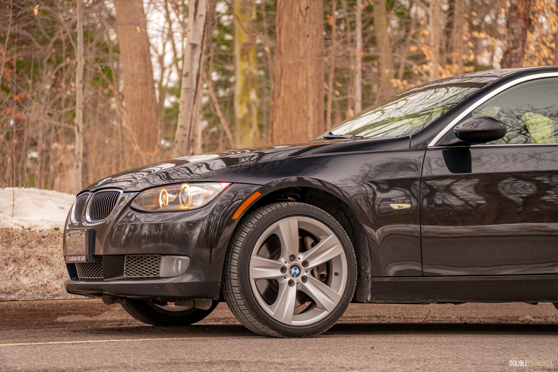 Front quarter view of a black 2008 BMW 335i Coupe on a cloudy day with trees in the background