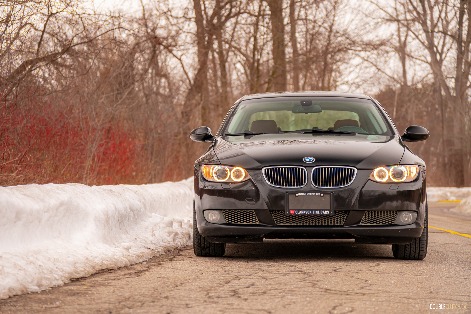 Front view of a black 2008 BMW 335i Coupe on a cloudy day with trees in the background