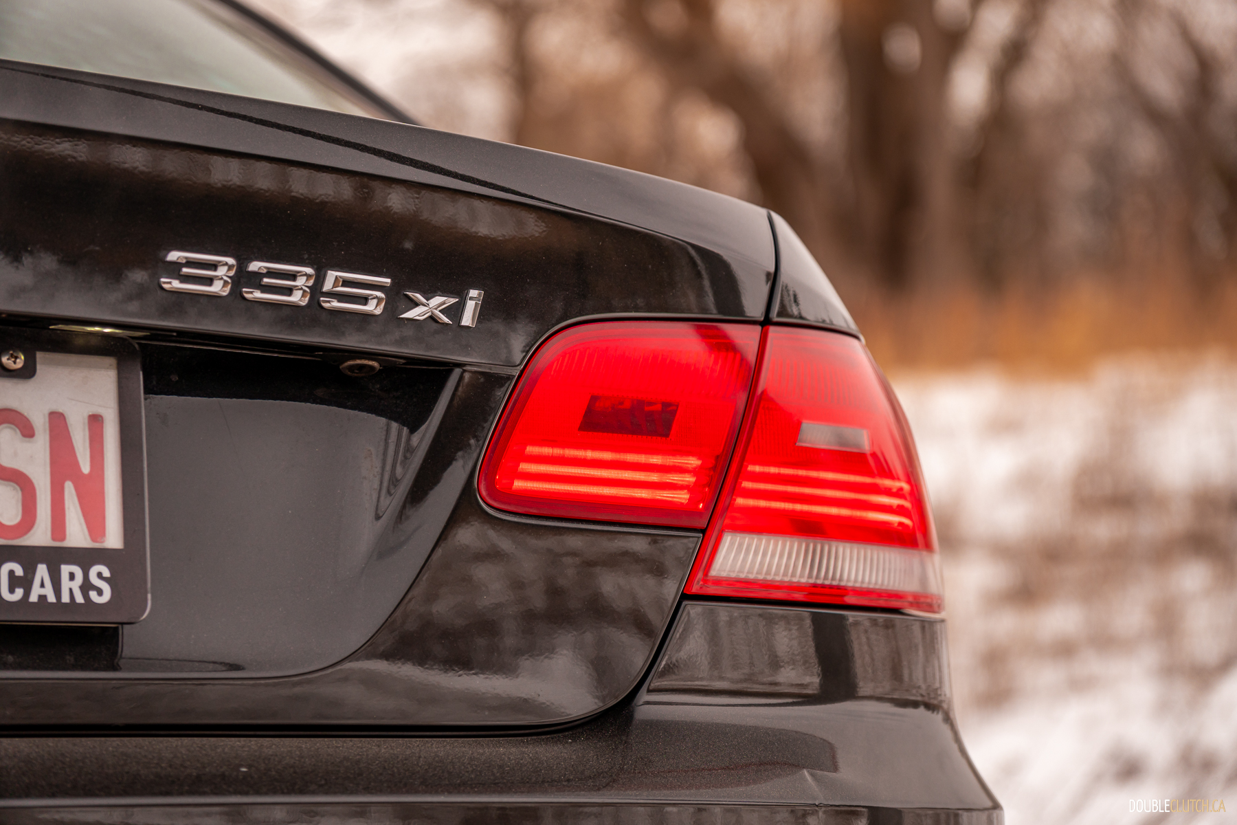 Close-up view of the badges on a black 2008 BMW 335i Coupe on a cloudy day with trees in the background
