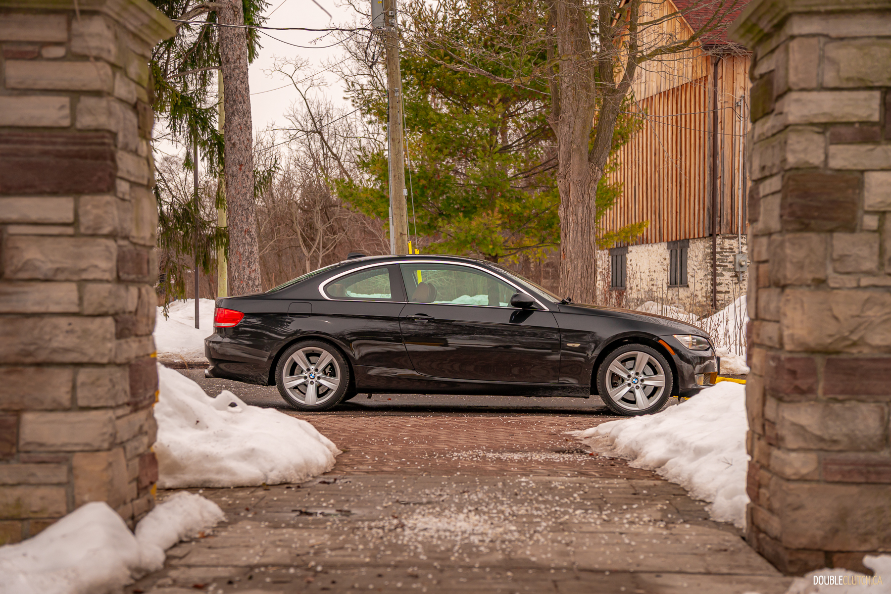 Side profile view of a black 2008 BMW 335i Coupe on a cloudy day with trees in the background