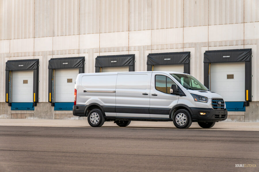 Front quarter view of a white 2025 Ford E-Transit with a warehouse in the background